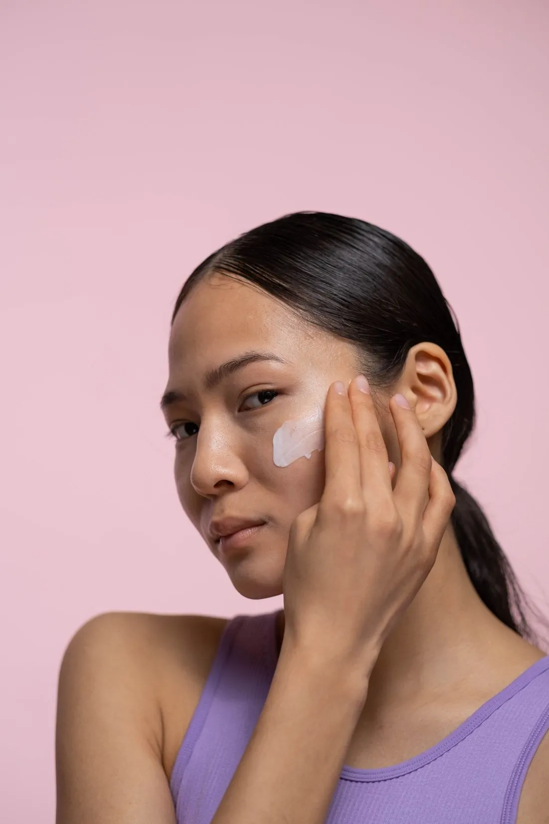 Cô gái chấm kem dưỡng lên gò má trước nền tường hồng